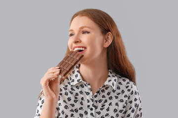 Young woman eating tasty chocolate on grey background, closeup