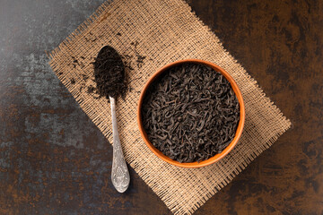 Dry black tea in a bowl and a spoon on a dark background