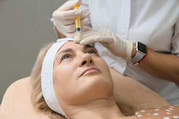 Cosmetologist makes facial mesotherapy to a mature woman.