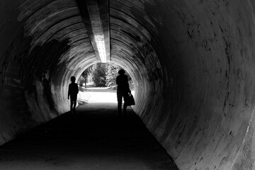 Grandmother and child in silhouettes in tunnel with dog waiting on the other side.