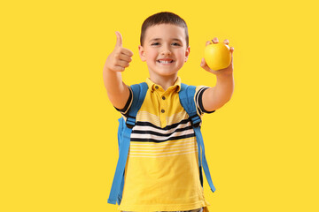 Little schoolboy with apple showing thumb-up on yellow background