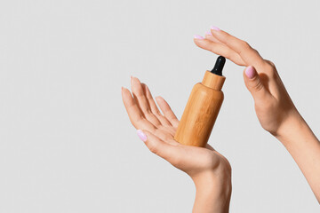 Hands of woman with bottle of cosmetic oil on light background