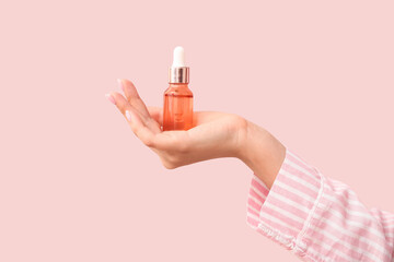 Hand of woman with bottle of cosmetic oil on pink background