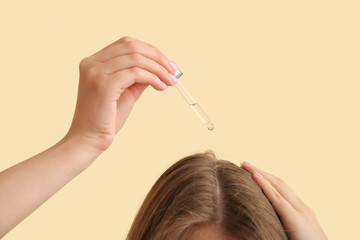 Young woman using cosmetic oil for hair treatment on beige background, closeup
