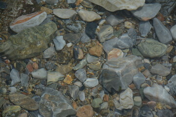 Multi-colored stones are visible from under the water on the sea