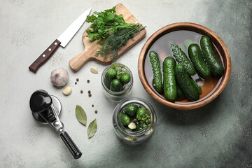 Jars and bowl with fresh cucumbers for preservation on grunge background