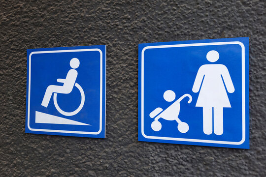 Sign of ramp for wheelchairs and prams on the wall of building. Symbol of person in wheelchair and mother with child in baby pram on blue square. Barrier-free concept.