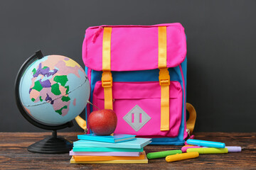 Backpack with different stationery and globe on wooden table against black chalkboard - Powered by Adobe