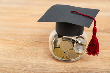 Jar with coins and graduation cap on wooden background. Student loan concept