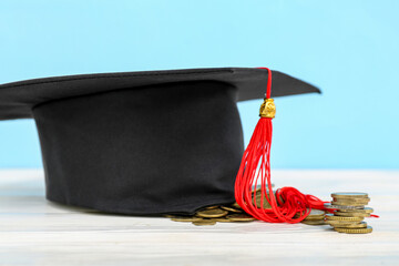 Graduation hat and stack of coins on white table against blue background. Student loan concept