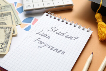 Notepad with text STUDENT LOAN FORGIVENESS and dollar banknotes on brown background, closeup