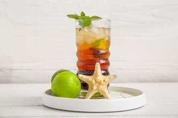 Fototapeta premium Plate with glass of cold Cuba Libre cocktail and starfish on white wooden background