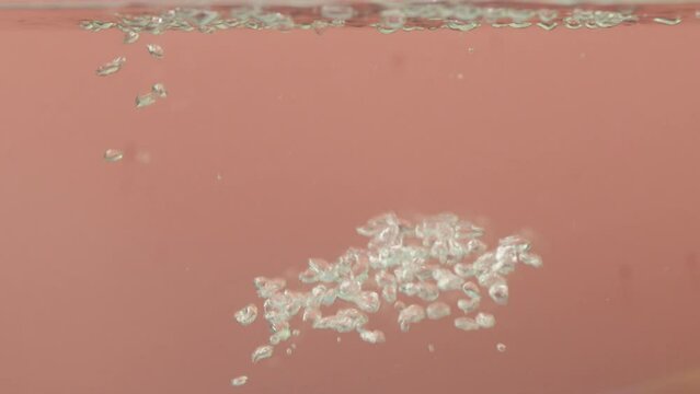 Air bubbles in the water rise upwards on a pink background. close up