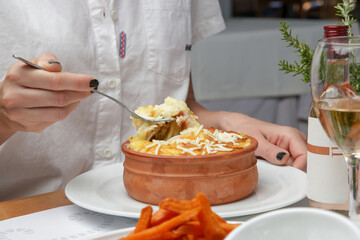 Woman eating traditional greek moussaka prepared in clay pot	
