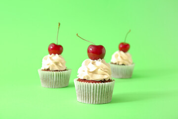 Tasty cherry cupcakes on green background