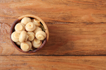 Bowl with canned mushrooms on wooden background