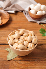 Bowl with canned mushrooms on wooden background