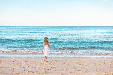 Girl in dress playing in waves on the beach. View from behind with no face and copy space.