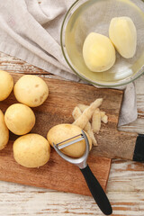 Board and bowl with raw potatoes on white wooden background
