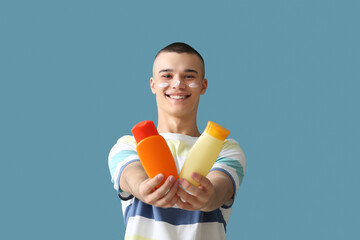 Happy young man with bottles of sunscreen cream on blue background