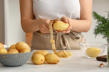 Woman peeling raw potatoes at table in kitchen