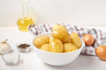 Bowl with raw potatoes on light background