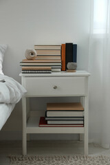 Hardcover books and scented candles on white bedside table indoors
