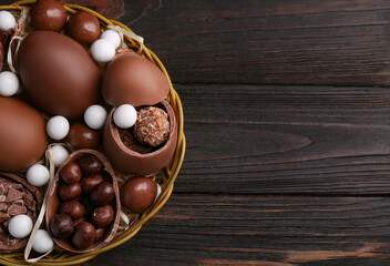 Fototapeta na wymiar Tasty chocolate eggs and sweets in wicker basket on wooden table, top view. Space for text