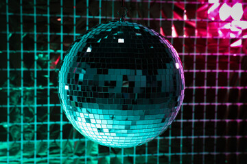 Shiny disco ball against foil party curtain under turquoise and pink light