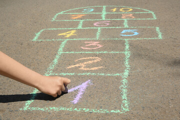 Child drawing hopscotch with colorful chalk on asphalt outdoors, closeup