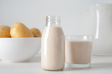 Bottle and glass of tasty potato milk on light background
