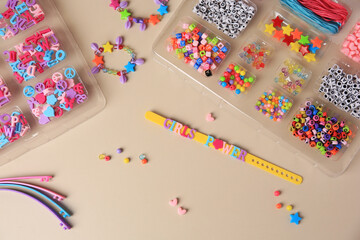 Fototapeta premium Handmade jewelry kit for kids. Colorful beads, and wristbands on beige background, flat lay