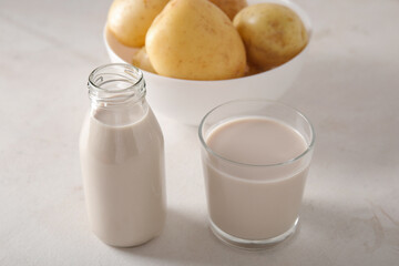 Bottle and glass of tasty potato milk on light background