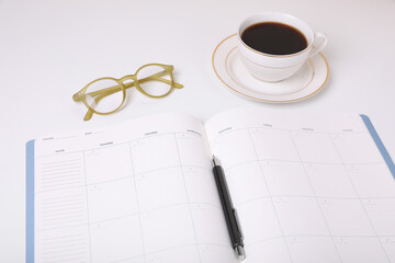 Open monthly planner, coffee, glasses and pen on white background