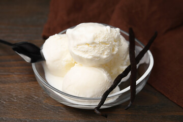 Delicious ice cream and vanilla pods in bowl on wooden table, closeup