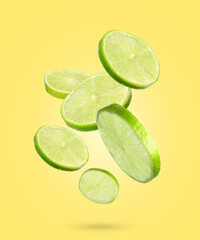 Fresh lime slices falling on yellow background