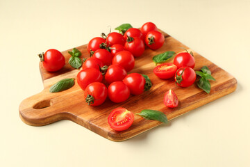 Wooden board with fresh cherry tomatoes and basil on light green background