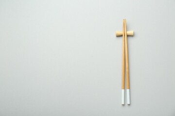 Pair of wooden chopsticks with rest on light grey background, top view. Space for text