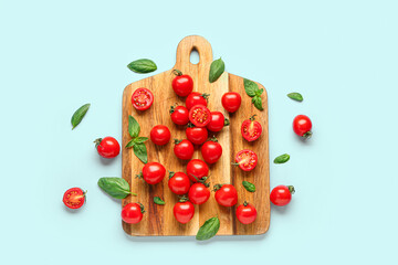 Wooden board with fresh cherry tomatoes and basil on blue background