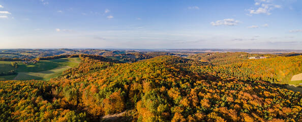 Aerial drone panoramic view of the autumn tree colors as the sun sets on the border of Burgenland and Styria in Austria under scattered clouds.