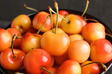 Bowl with sweet yellow cherries on black background, closeup