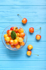 Bowl with fresh yellow cherry on blue wooden background