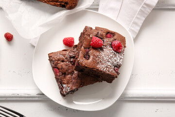 Plate with pieces of raspberry chocolate brownie on white background