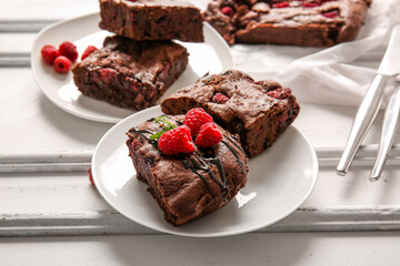 Plates with pieces of raspberry chocolate brownie on white background