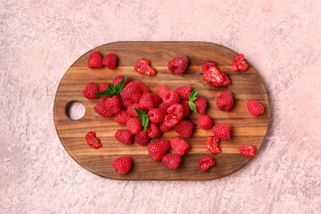 Wooden board with fresh raspberries and mint on pink background