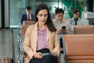 Businesswoman checking flight boarding passes.People sitting on airport chairs waiting to board the plane.