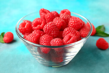Glass bowl with fresh raspberries on blue background