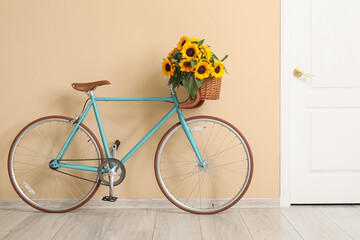 Bicycle with bouquet of beautiful sunflowers in wicker basket near beige wall