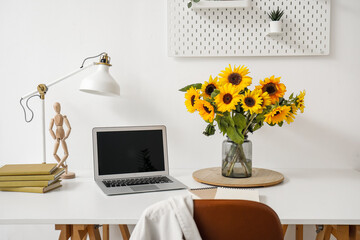 Vase with beautiful sunflowers and modern laptop on white table, closeup