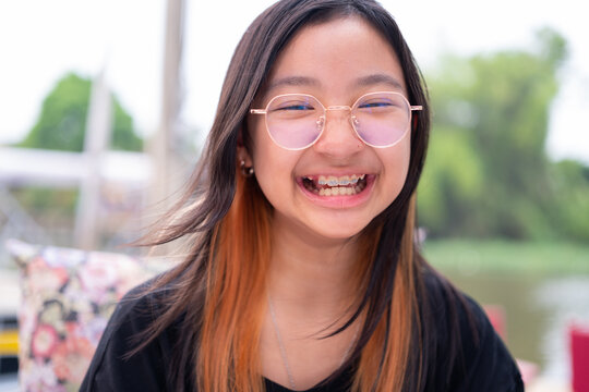 Asian girl teenage girl with braces and eyeglasses wearing black t-shirt smiling brightly on background outdoors.